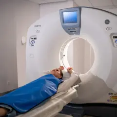 Pacjentka leży na stole tomografu komputerowego, przygotowana do badania. Widoczny jest nowoczesny sprzęt medyczny, który pozwala na szczegółowe obrazowanie wnętrza ciała, wyjaśniając, jak działa tomografia komputerowa.