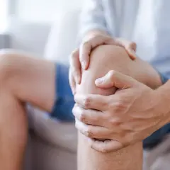 Mężczyzna trzyma się za kolano, odczuwając ból. Przyczyny bólu kolana mogą być różne, od urazów po choroby zwyrodnieniowe.