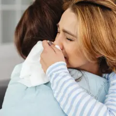 Kobieta pociesza inną, która płacze, wycierając nos chusteczką. Scena sugeruje lęk separacyjny u dorosłych i potrzebę wsparcia.