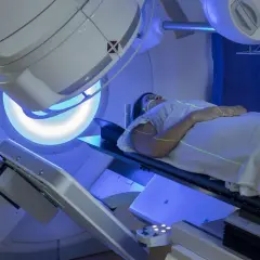 Pacjentka leży na stole terapeutycznym, a nad nią znajduje się urządzenie do radioterapii. Zielone linie lasera pomagają w precyzyjnym ustawieniu. Tak wygląda na czym polega radioterapia.