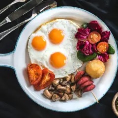 Pyszne śniadanie z jajkami sadzonymi, pomidorami, grzybami i sałatką. Czy jajka podnoszą cholesterol? To pytanie nurtuje wielu, ale ten talerz wygląda apetycznie!
