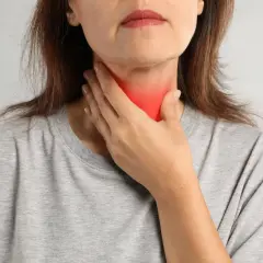 Kobieta dotyka szyi z zaczerwienieniem, co może symbolizować problemy z tarczycą, takie jak niedoczynność tarczycy a menopauza.