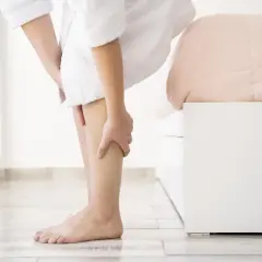 Osoba w szlafroku masuje łydkę, cierpiąc z powodu bólu łydek w nocy.