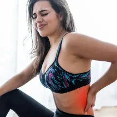 Kobieta w sportowym topie odczuwa mrowienie w plecach, trzymając się za bolący bok.