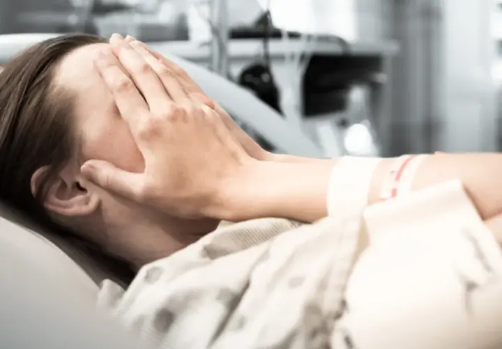 Osoba w szpitalu zakrywa twarz dłońmi. Zastanawia się, w jakim wieku zawał jest najgroźniejszy.