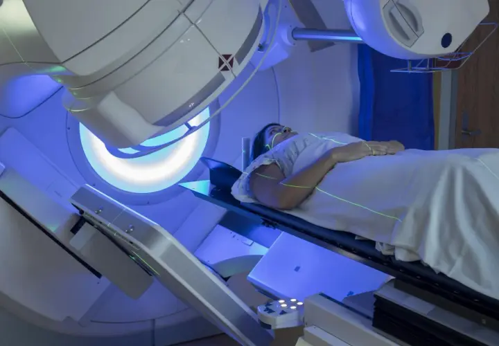 Pacjentka leży na stole terapeutycznym, a nad nią znajduje się urządzenie do radioterapii. Zielone linie lasera pomagają w precyzyjnym ustawieniu. Tak wygląda na czym polega radioterapia.