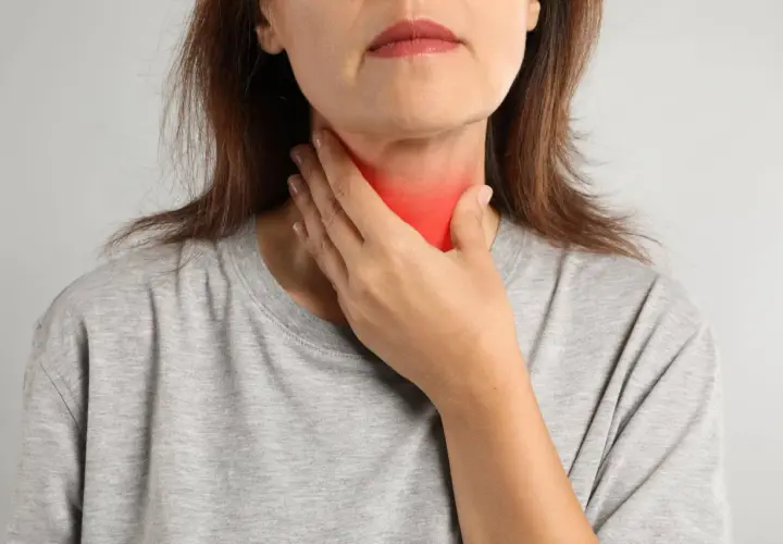 Kobieta dotyka szyi z zaczerwienieniem, co może symbolizować problemy z tarczycą, takie jak niedoczynność tarczycy a menopauza.