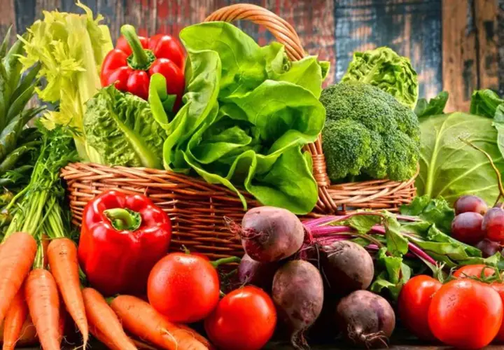 Koszyk pełen świeżych warzyw i owoców, idealnych na dietę owocowo warzywną: ananas, banany, marchew, papryka, pomidory, buraki, sałata, brokuły, kapusta, winogrona.
