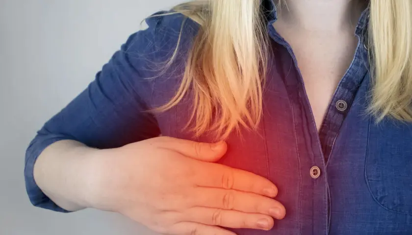 Kobieta z blond włosami trzyma rękę na piersi, odczuwając ból. Czy torbiel w piersiach może pęknąć?