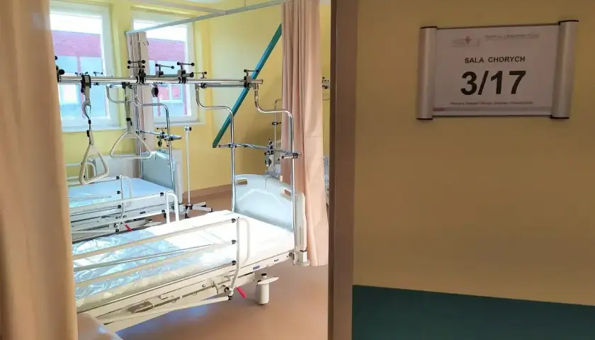Szpitalna sala chorych z dwoma łóżkami i aparaturą medyczną.