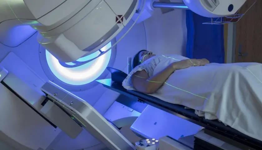 Pacjentka leży na stole terapeutycznym, a nad nią znajduje się urządzenie do radioterapii. Zielone linie lasera pomagają w precyzyjnym ustawieniu. Tak wygląda na czym polega radioterapia.