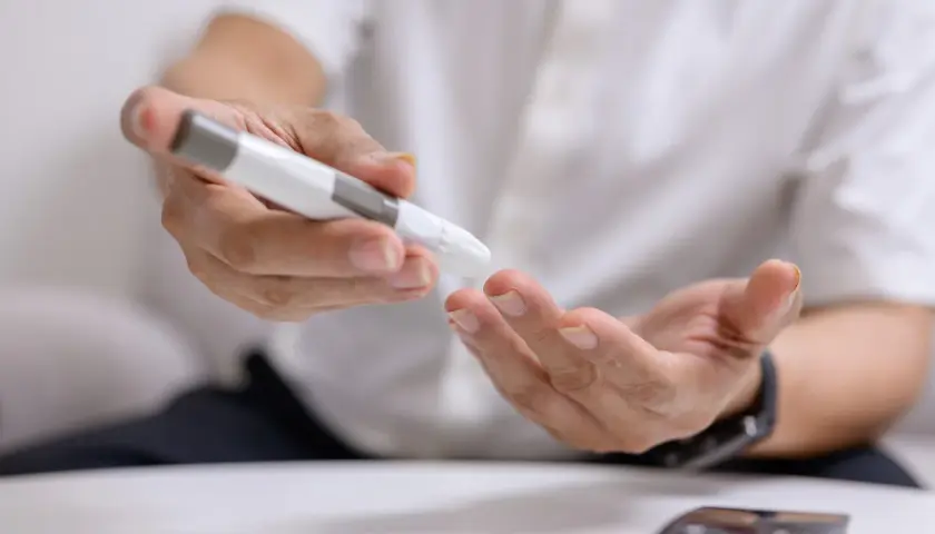 Osoba wykonuje badanie kodu metabolicznego, używając glukometru do nakłucia palca.