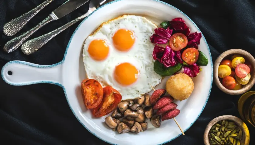 Pyszne śniadanie z jajkami sadzonymi, pomidorami, grzybami i sałatką. Czy jajka podnoszą cholesterol? To pytanie nurtuje wielu, ale ten talerz wygląda apetycznie!