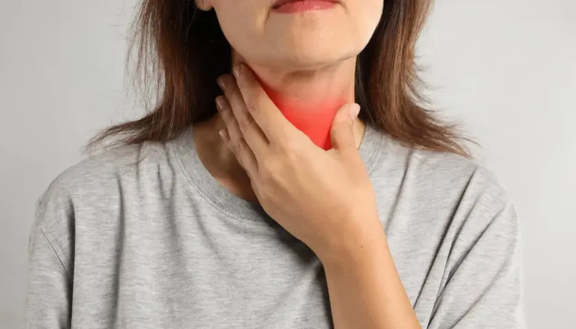 Kobieta dotyka szyi z zaczerwienieniem, co może symbolizować problemy z tarczycą, takie jak niedoczynność tarczycy a menopauza.