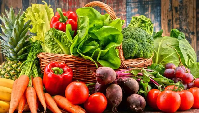 Koszyk pełen świeżych warzyw i owoców, idealnych na dietę owocowo warzywną: ananas, banany, marchew, papryka, pomidory, buraki, sałata, brokuły, kapusta, winogrona.