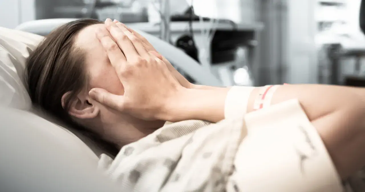 Osoba w szpitalu zakrywa twarz dłońmi. Zastanawia się, w jakim wieku zawał jest najgroźniejszy.