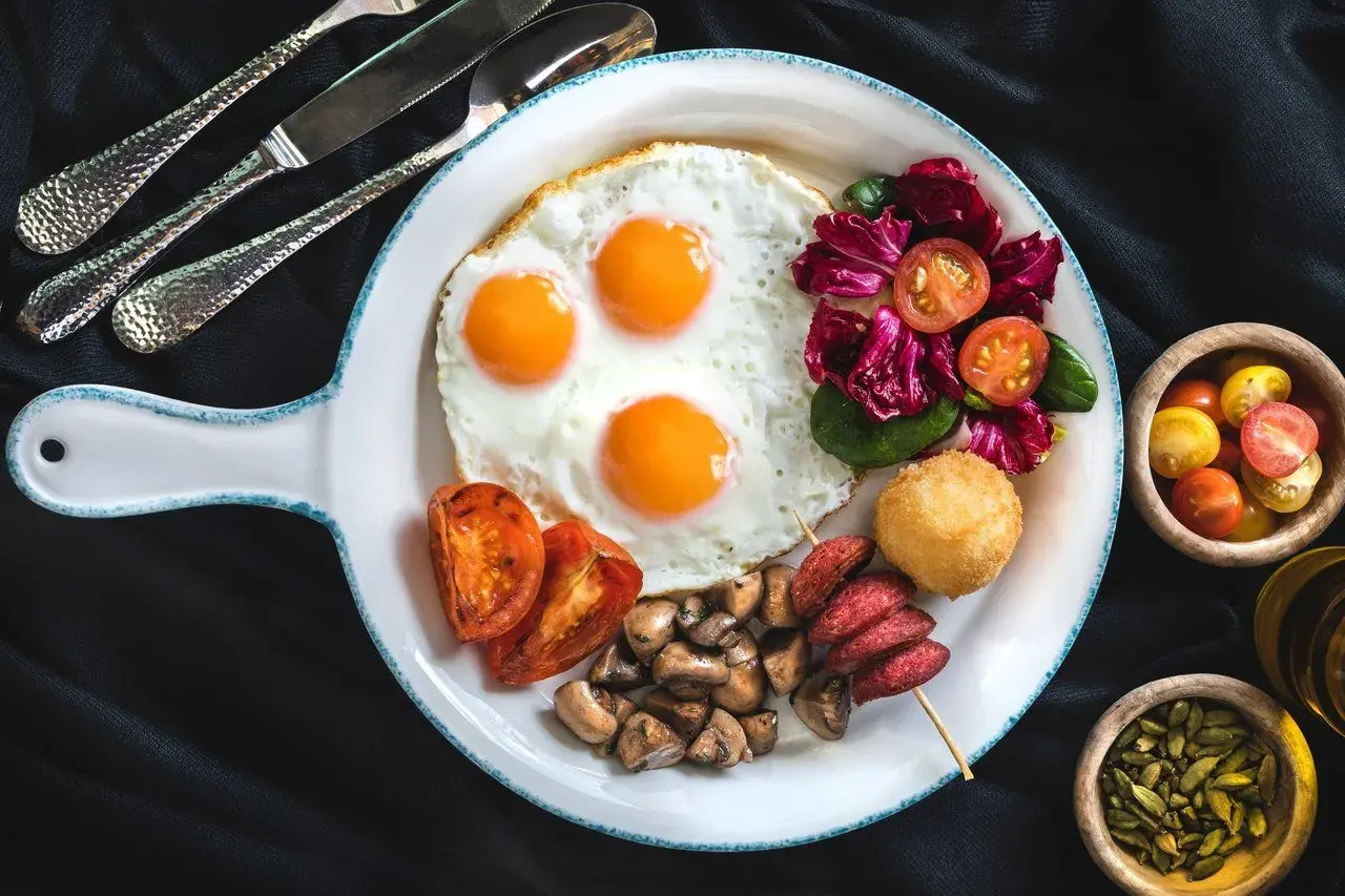 Pyszne śniadanie z jajkami sadzonymi, pomidorami, grzybami i sałatką. Czy jajka podnoszą cholesterol? To pytanie nurtuje wielu, ale ten talerz wygląda apetycznie!