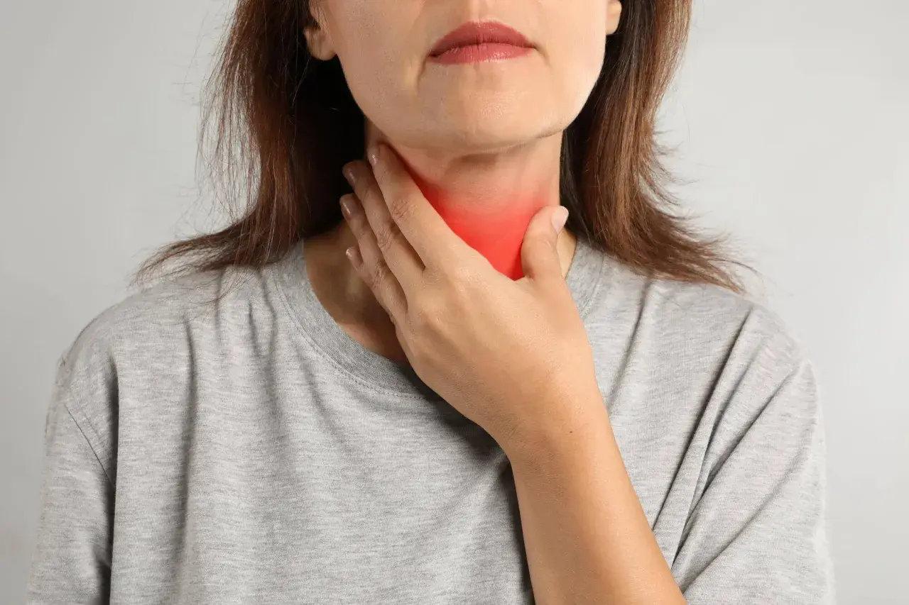 Kobieta dotyka szyi z zaczerwienieniem, co może symbolizować problemy z tarczycą, takie jak niedoczynność tarczycy a menopauza.