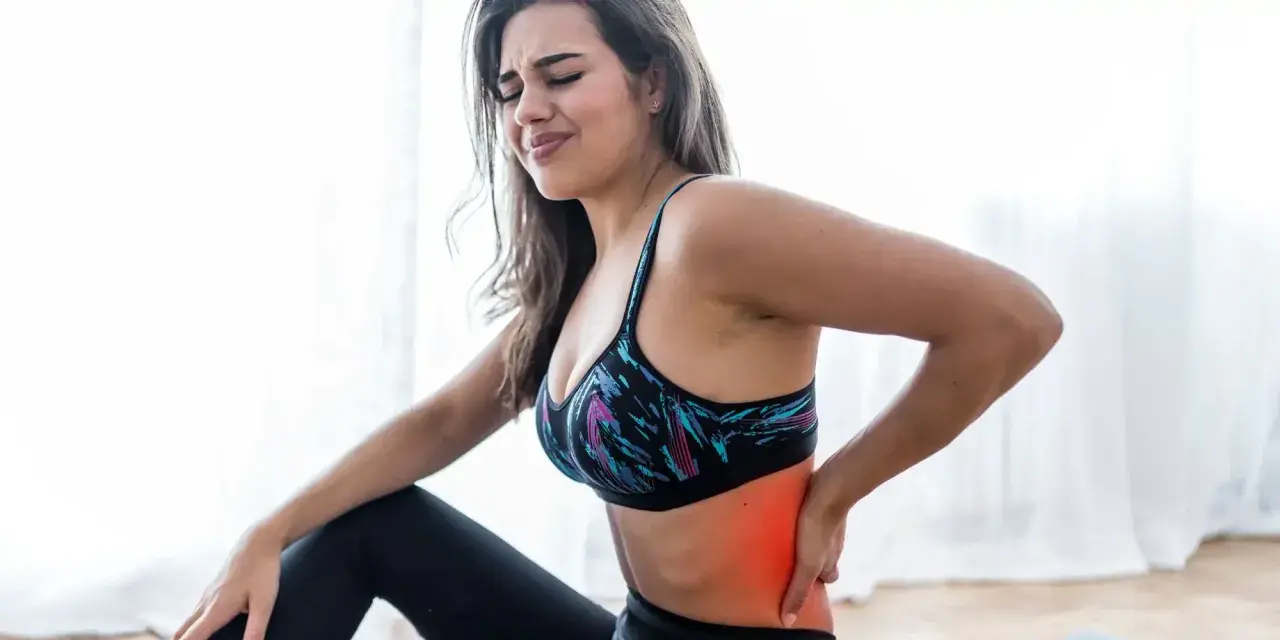 Kobieta w sportowym topie odczuwa mrowienie w plecach, trzymając się za bolący bok.