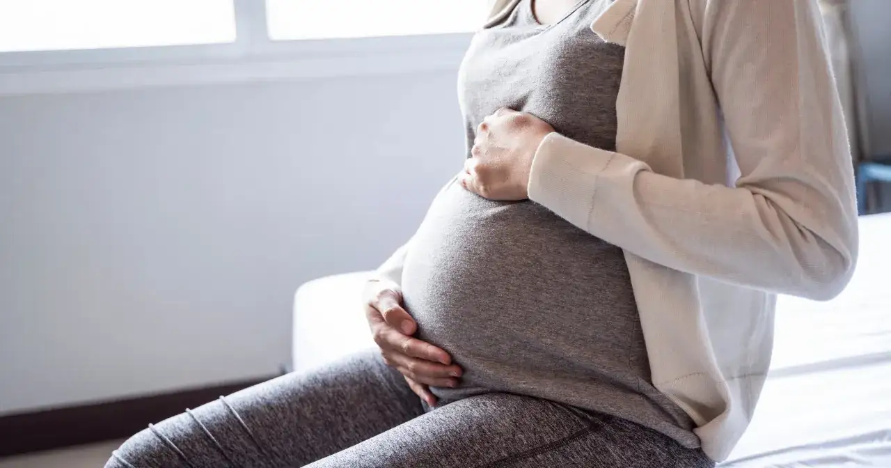 Kobieta w ciąży trzyma się za brzuch, odczuwając ból związany z kolką jelitową.