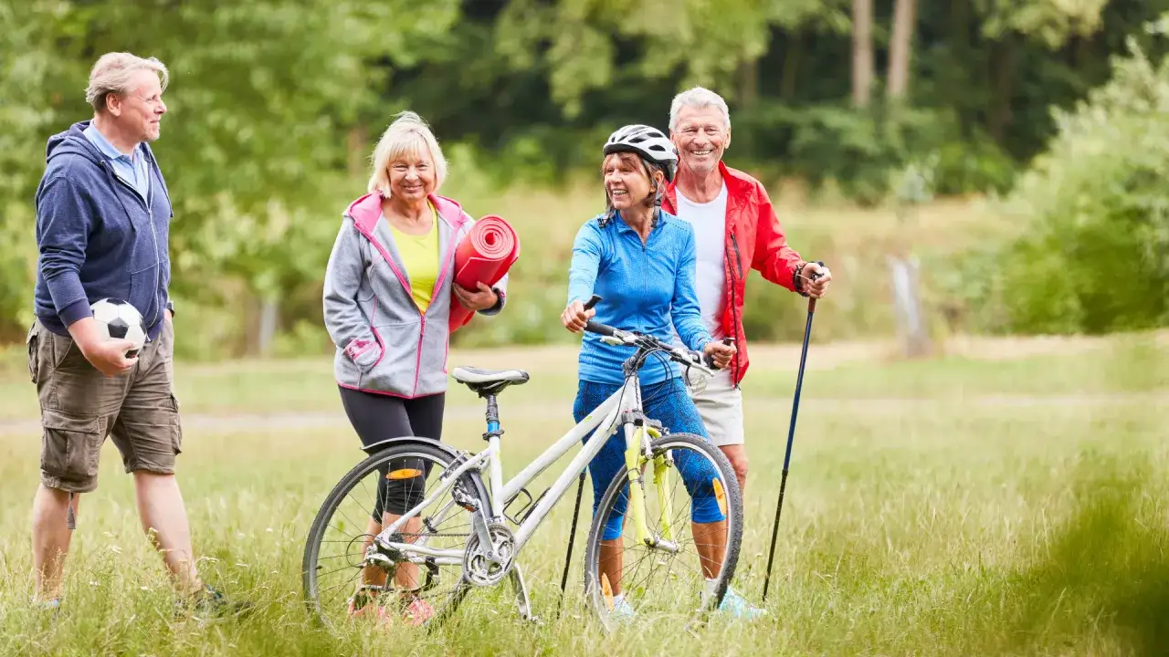 Aktywni seniorzy gotowi na trening umysłu i ciała: rower, piłka, mata do ćwiczeń i kijki trekkingowe.