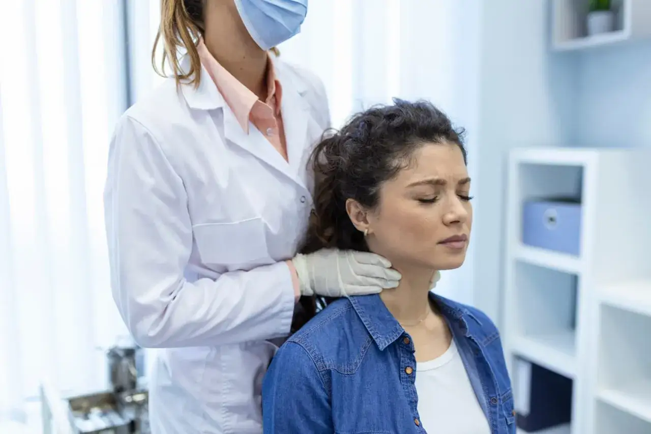 Lekarz bada szyję pacjentki, co może być związane z problemami tarczycy, takimi jak niedoczynność tarczycy a menopauza.