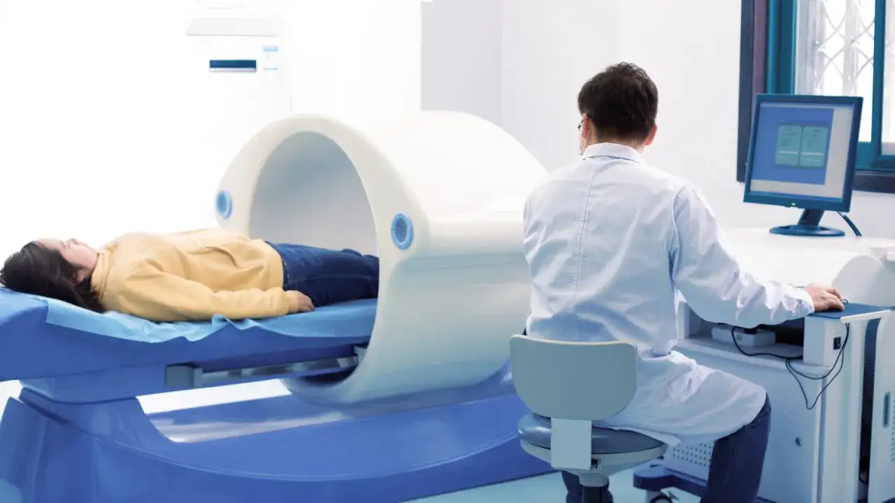 Pacjentka leży w aparacie do densytometrii. Lekarz przy komputerze monitoruje badanie. Densytometria ile trwa? Krótko i bezboleśnie.