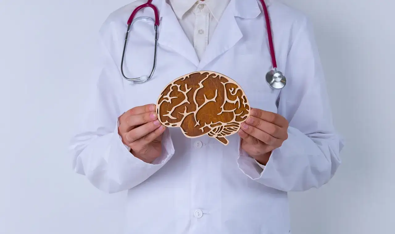 Lekarz w białym kitlu trzyma drewniany model mózgu, symbolizujący zrozumienie problemów neurologicznych, takich jak padaczka nieświadomości u dorosłych.