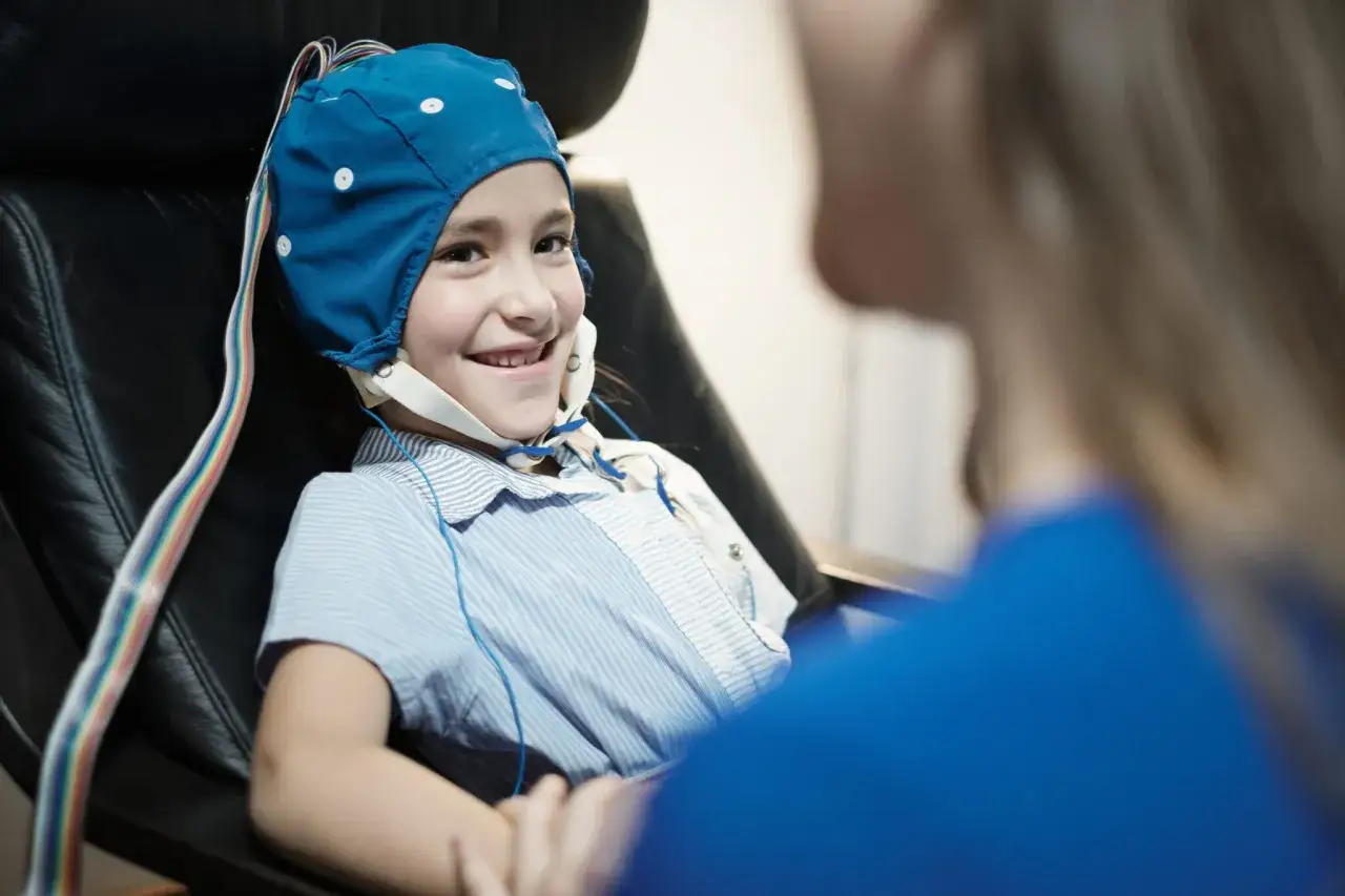 Uśmiechnięta dziewczynka w czepku z elektrodami do EEG, gotowa na badanie pod kątem zmian napadowych w eeg.