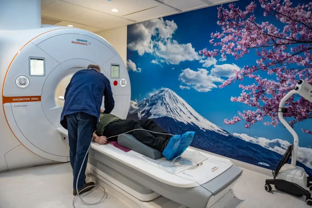 Pacjent leży na łóżku rezonansu magnetycznego, przygotowywany do badania. Obrazek pokazuje, jak działa tomografia komputerowa, tworząc szczegółowe przekroje ciała.