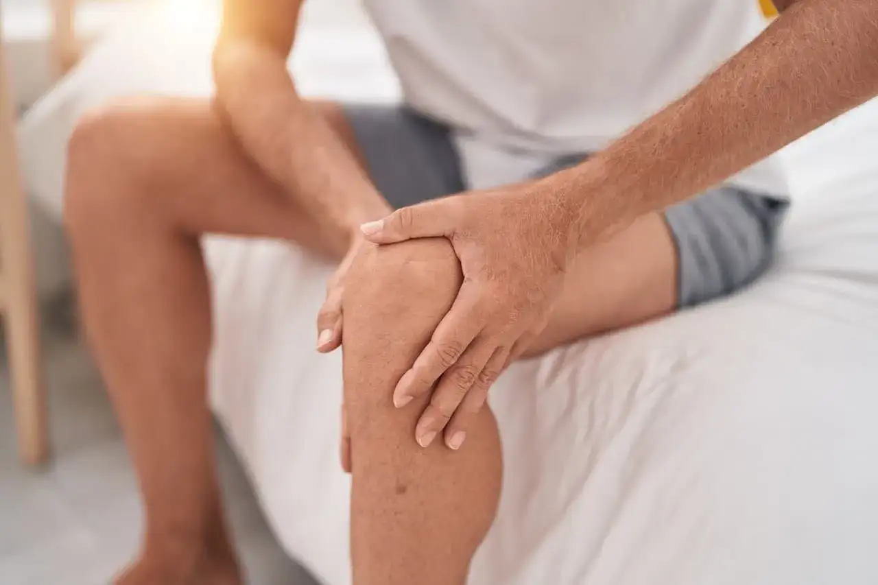 Mężczyzna trzyma się za bolące kolano, co może być objawem osteoartrozy.