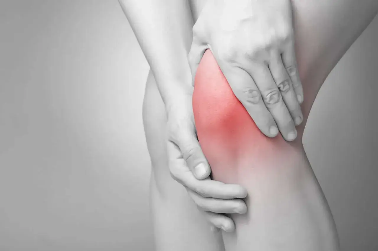Dłoń uciska bolące kolano, gdzie widać zaczerwienienie. To może być objaw osteoartrozy, czyli choroby zwyrodnieniowej stawów.