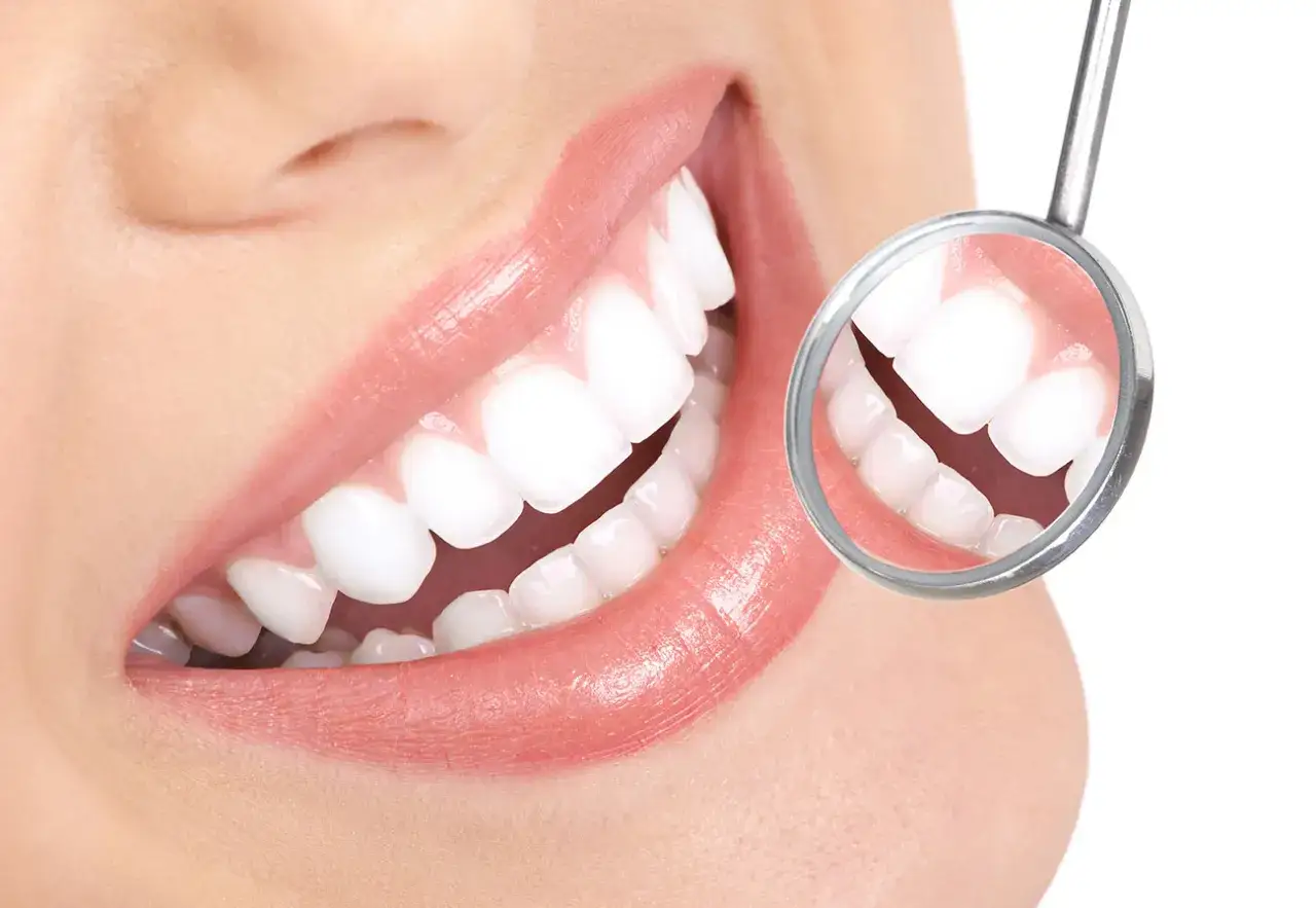 Uśmiech z idealnie białymi zębami, widocznymi w lusterku dentystycznym. Płukanie ust olejem lnianym dla zdrowia jamy ustnej.